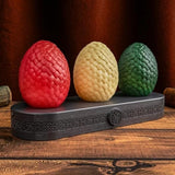 Three dragon eggs in red, yellow, and green on a dark stand with a wooden background