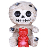 Mummy figurine holding a red gummy bear on a white background