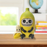 Skull-shaped toy with a banana body on a desk with books and a globe in the background