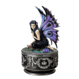 Decorative figurine of a fairy with purple wings on top of a decorative box.