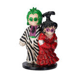 Two colorful figurines, one with green hair and zebra-striped outfit, the other with black hair and red dress, on a white background.