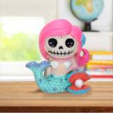 Skull mermaid figurine with pink hair and blue tail on a wooden surface.