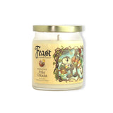 A glass jar candle with a gold metal lid and cream-colored wax, featuring a label for 'Feast of Santafé Candles' in the scent 'Pina Colada'. The label has a vintage illustration of a guinea pig in a basket surrounded by tropical fruits.