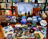 Board game 'Expeditions' with various cards and figures on a table, surrounded by books.