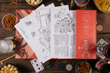 Open book with game-related pages on a wooden table with snacks and drinks.