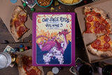 Book titled 'One-Page RPGs Volume 3' on a table with pizza slices and gaming accessories.