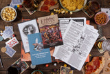 Tabletop gaming session with gaming books, cards, and snacks on a wooden table.