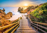 Wooden staircase leading to a beach with rock formations and a sunset.