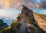 Stairway leading up a rocky cliff with a scenic view of clouds and mountains.