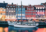 Colorful buildings along a waterfront with boats docked in front, illuminated by evening lights.