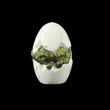 Decorative figurine of a green dragon emerging from a white egg on a black background