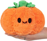 Plush pumpkin toy held in a hand with a white background