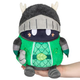 Plush toy resembling a dragon in a knight's outfit held in a hand against a white background