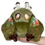 Green plush toy with patches held by a hand on a white background