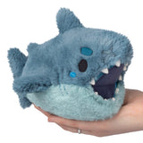 Blue plush toy resembling a shark held in a hand on a white background