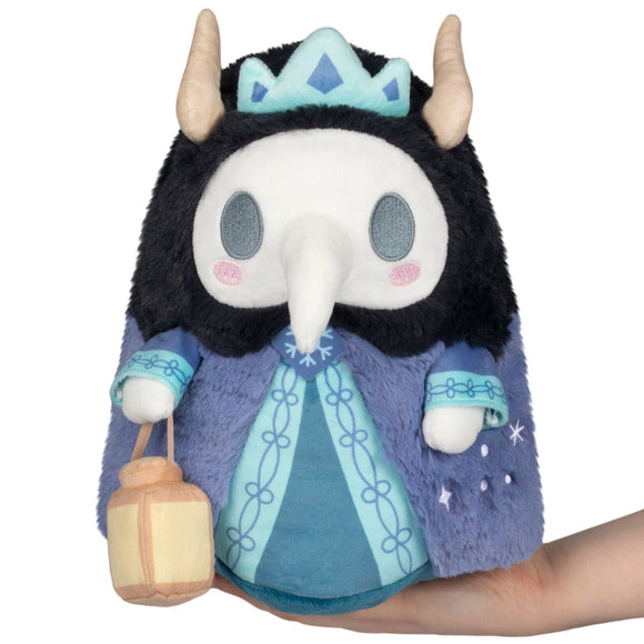 Plush toy with a black hood, blue dress, and crown held by a hand on a white background