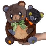 Two plush toys, one brown bear and one black cat, held by a hand on a white background.