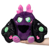Purple plush toy with black ears and green eyes held by a hand on a white background