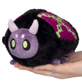 Plush toy resembling a black and purple creature with horns held in a hand on a white background