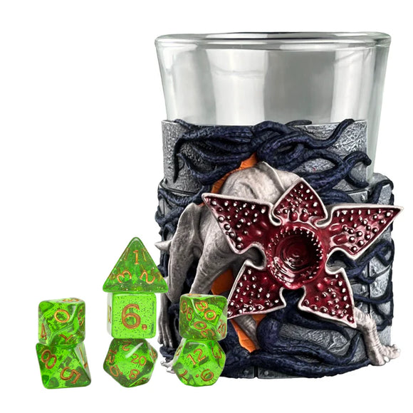 Decorative shot glass with a dragon design, surrounded by green dice on a white background