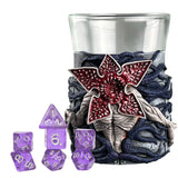 Decorative glass with a red flower design, surrounded by purple dice on a white background