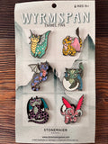 Packaged set of Wyrmspan enamel pins with dragon designs on a wooden surface.