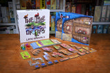Board game components including cards and pieces on a wooden table with game box in the background.