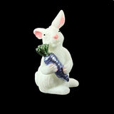 White ceramic rabbit holding a purple carrot on a black background