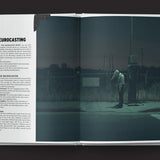 Open book showing a dark, moody scene with a person near a control panel.