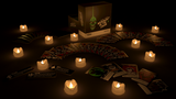 Darkly lit scene with candles, cards, and a box on a dark surface