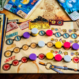 A close-up of a board game board with colorful player tokens, ticket-like cards, and game components arranged on a vintage-style printed board. No person or animal is visible, but this is not a clean isolated studio product shot; it is shown in a real tabletop setting, so Lifestyle fits better than Product/Packaging.