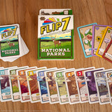 The Flip 7 National Parks card game set arranged on a wooden tabletop, showing the main box, a deck of cards, several individual cards, and additional cards fanned out in front.