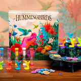 Colorful 'Hummingbirds' board game set with game pieces and box on a wooden surface.