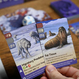 Two game cards featuring animals on a wooden surface with other cards in the background.