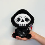 Plush toy resembling a skull with a heart saying 'I'd Kill for You' held by a hand against a white background
