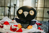 raven plush holding a black heart with text sitting on a table