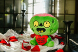Green zombie plush toy with a heart saying 'I love you for your brain' on a white surface with red roses.