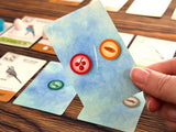 Hand holding a card with icons on a table with other cards