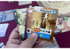 Hand holding a board game card with illustrations and text, surrounded by other game cards.