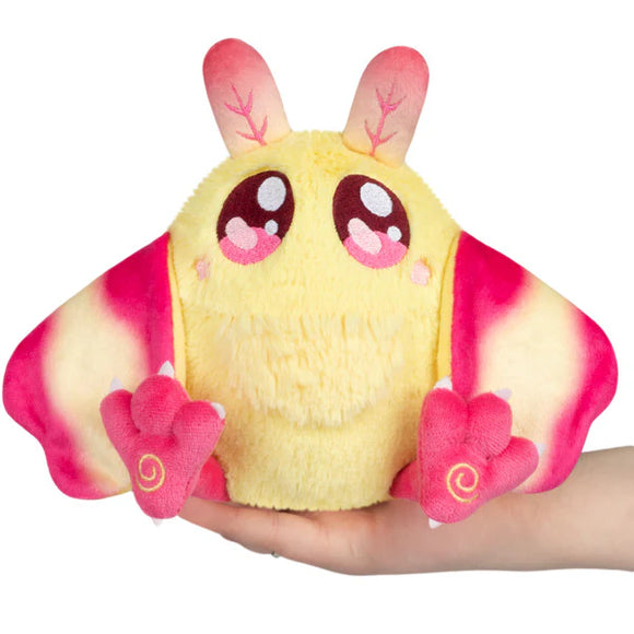Plush toy moth with yellow body and pink wings held in a hand on a white background