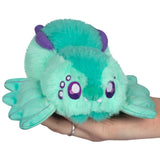 Green plush toy with purple accents held in a hand on a white background