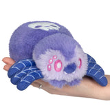 Purple plush toy resembling a spider on a hand against a white background