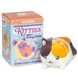 A squishable 'Kitties Series 1: Cozy Cats' mystery plush keychain shown next to its retail packaging box. The plush toy is a calico cat design with white, orange, and dark brown sections, and a silver metal keychain ring on its head.