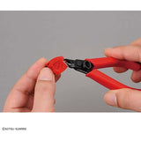 Red pliers with a small red clip being held by hands against a gray background