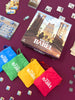 Board game 'Rise of Babel' with colorful drawstring bags on a purple surface.