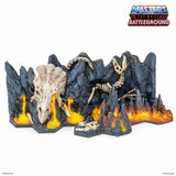 Toy battleground set with skeletons and flames, featuring 'Masters of the Universe' branding.