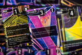 A close-up of a colorful trading card with abstract neon artwork in pink, purple, blue, and yellow, with other cards blurred in the background.
