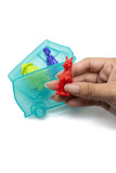 Hand holding a red toy figure next to a transparent blue container with colorful figures inside on a white background