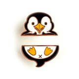 A penguin-themed enamel pin shown in two separated pieces on a white background. The top half shows the penguin's head with black, white, and yellow detailing, and the bottom half shows the lower body with yellow feet and a small black X.