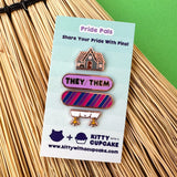 Set of pride-themed pins on a card with 'Kitty with a Cupcake' branding, placed on a straw background.